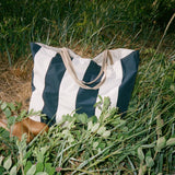 Shore Carryall striped bag resting beside coastal plants